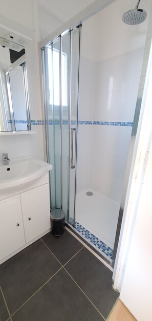 A bathroom with a glass-enclosed shower, a white sink, and a tiled floor.