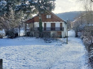 A two-story house with a stone facade, a balcony, and a snow-covered yard.