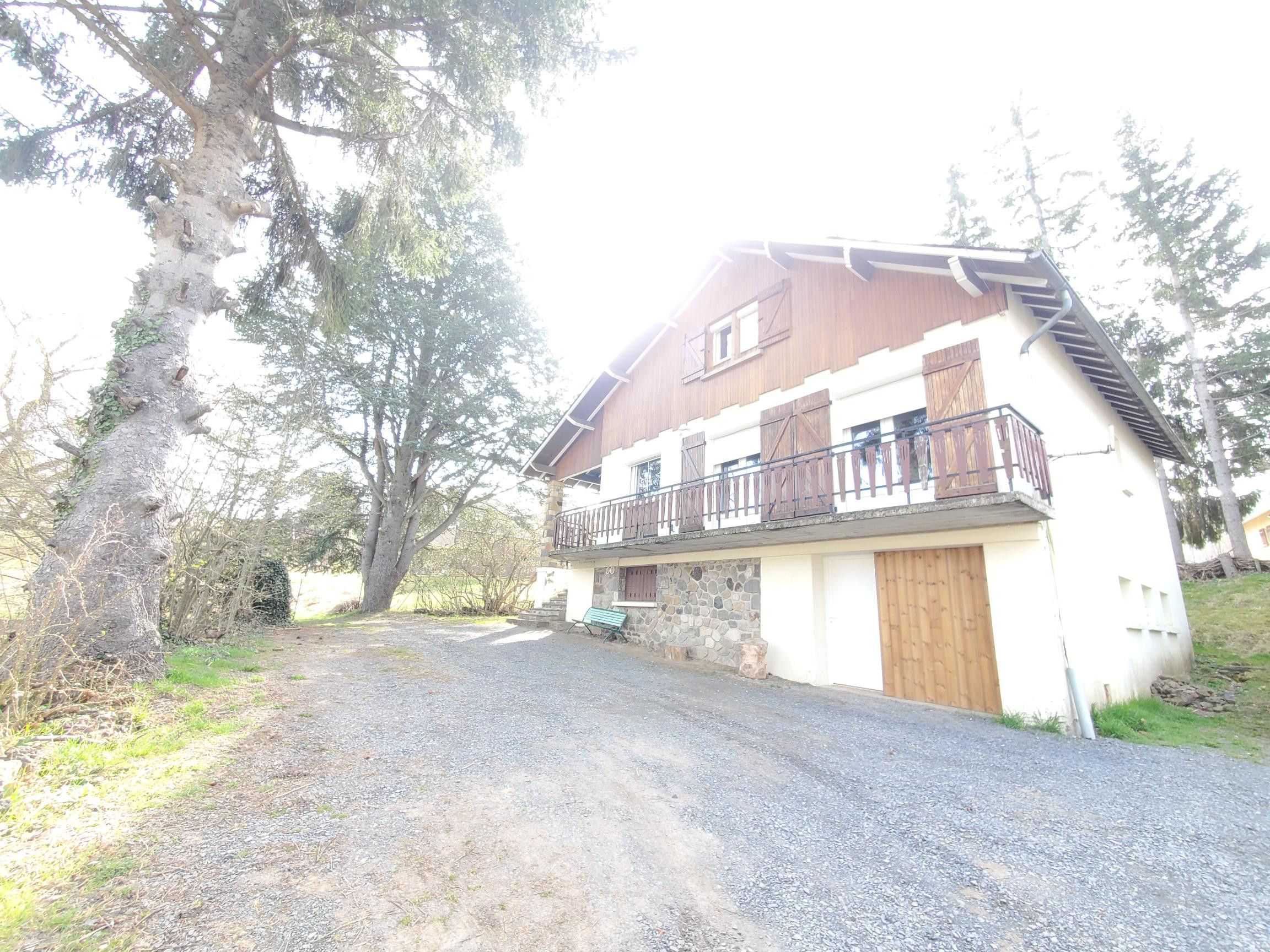 A two-story house with a stone foundation, a wooden balcony, and a gravel driveway.