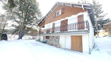 Un chalet à deux étages avec une façade en pierre, des volets en bois et un balcon doté de rampes en métal.