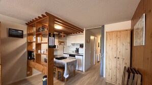 A compact kitchen with wooden shelves, a dining table, and a small island.