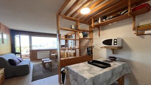 A cozy living room with a sofa, a dining table with a tray, and a kitchen area with wooden shelves and a microwave.
