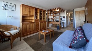 A compact living space with a kitchenette, wooden cabinets, a dining area, and a sofa with a patterned pillow.