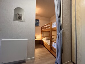 Une chambre avec des lits superposés, un radiateur, une petite table avec une lampe et un tableau accroché au mur.