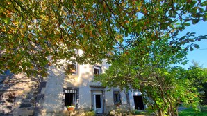 Ein rustikales Steinhaus mit Garten, einem kleinen Tisch und einem Baum im Vordergrund.