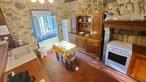 Eine rustikale Küche mit Steinwänden, Holzschränken, gefliestem Boden, einem Kühlschrank, einem Herd und einem Fenster mit Gitterstäben.