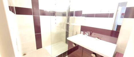 Un baño moderno con ducha de vidrio, lavamanos blanco y baldosas de tonos oscuros.