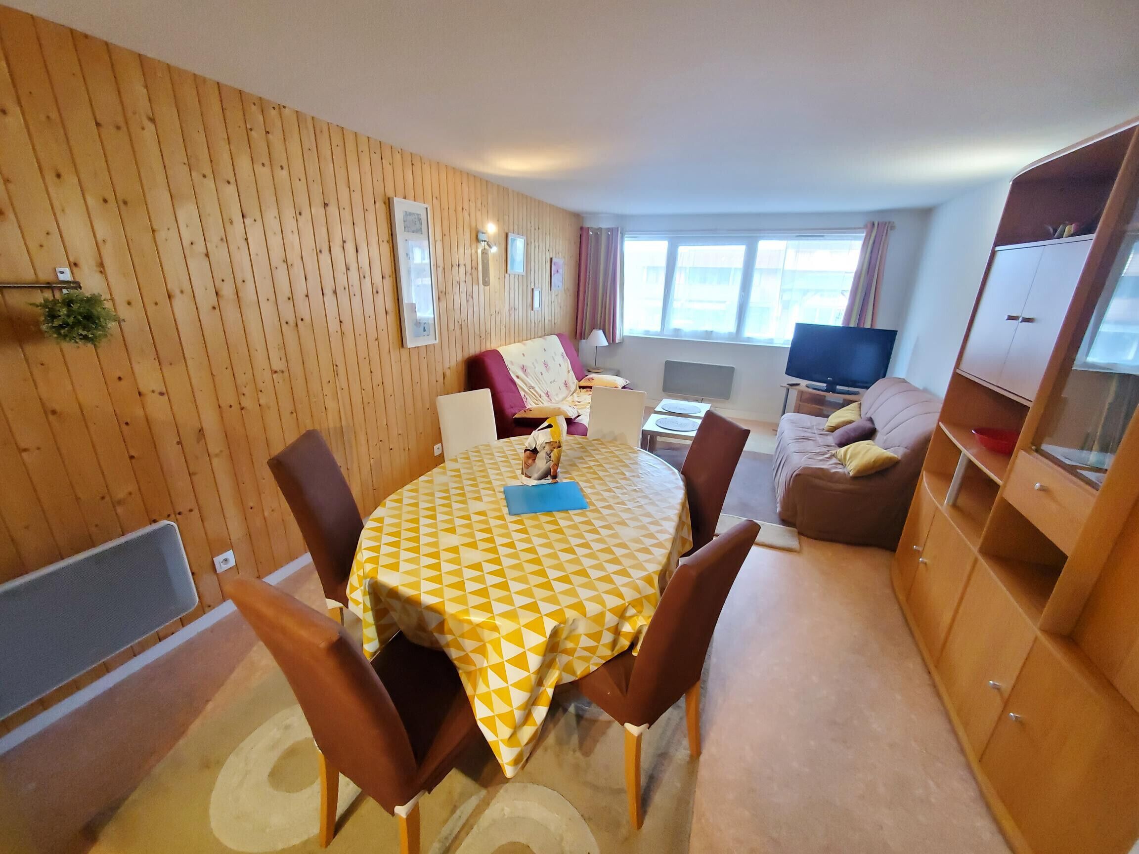Una habitación acogedora con un revestimiento de madera, una mesa de comedor con sillas, un sofá, un televisor y un armario.