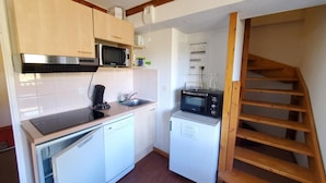 A compact kitchen with a microwave, coffee maker, and dishwasher. There is a wooden staircase leading to an upper level.