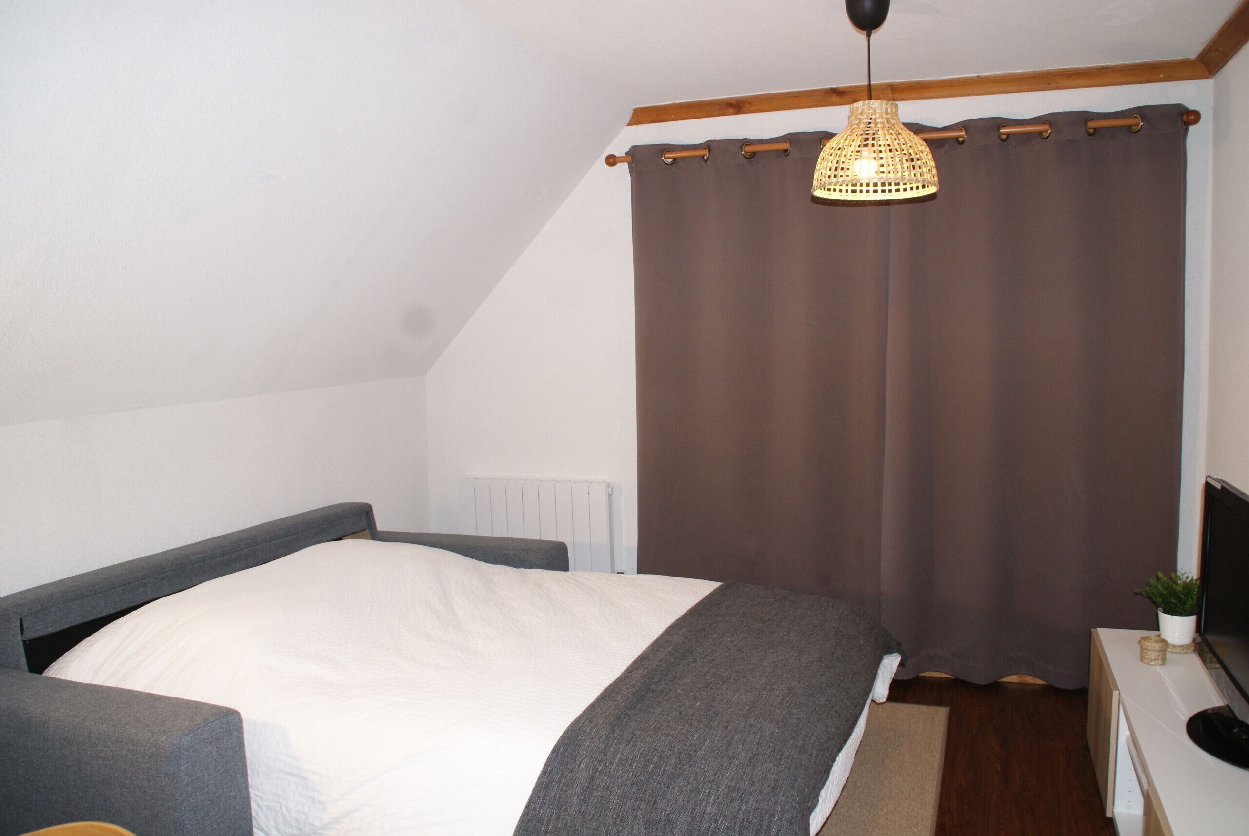 Un dormitorio con cama, mesita de noche, televisor y ventana con cortinas.