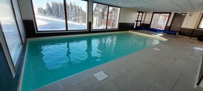 Una piscina interior con ventanales que ofrecen vistas a un paisaje nevado y edificios.
