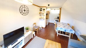 Un espai habitable compacte amb televisió, zona de seients, taula de dinar, cuina i un rellotge a la paret.