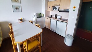 A compact kitchen with a white countertop, a microwave, a coffee maker, and a dishwasher. There are wooden chairs around a small dining table. - 4145a (Besse-et-Saint-Anastaise)
