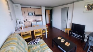 A compact living space with a kitchenette, a dining area, a sofa, a TV, and a small table with trays. - 4145a (Besse-et-Saint-Anastaise)