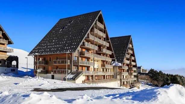 Un bâtiment moderne abritant une station de ski, doté de nombreux balcons et d’un toit en pente.