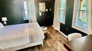 Ein Schlafzimmer mit Bett, Schreibtisch, Kommode und Fenster.