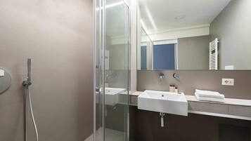 Un baño moderno con cabina de ducha de vidrio, un lavabo blanco y un espejo sobre él.