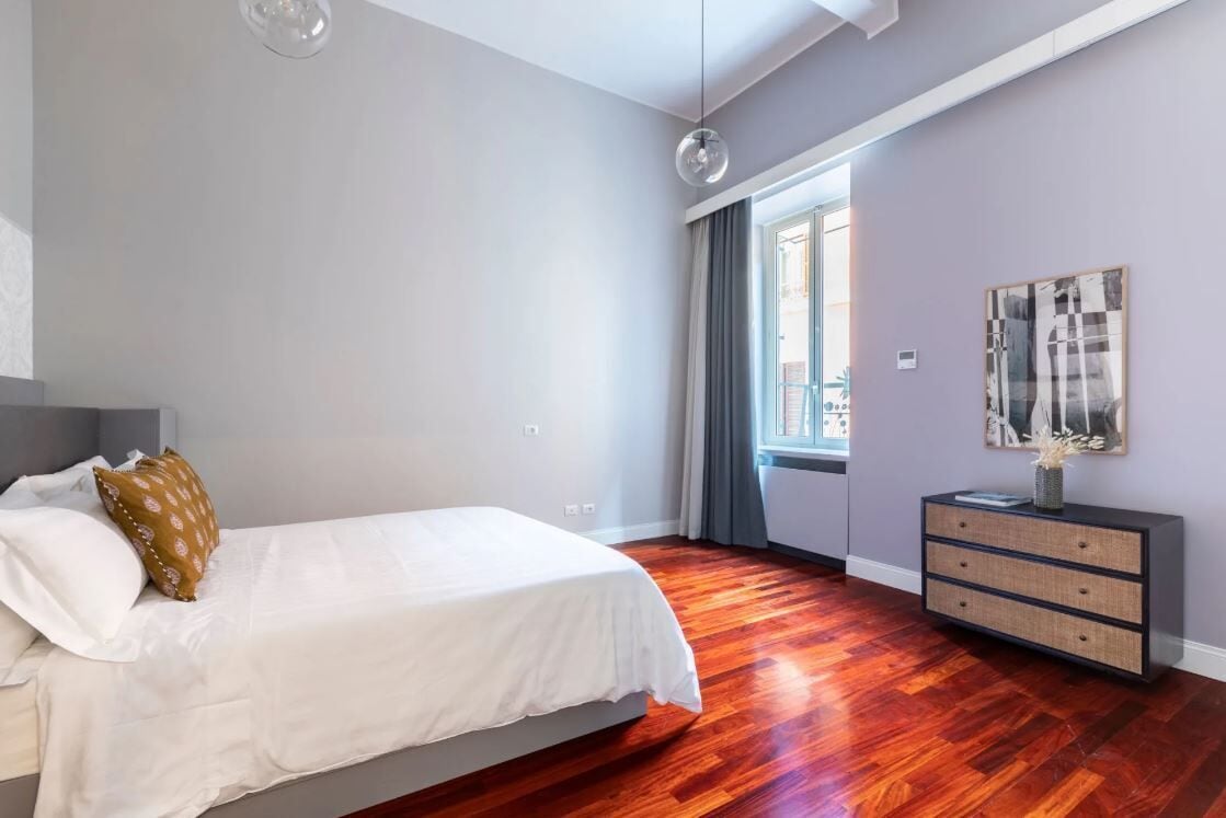 A modern bedroom with a large bed, a dresser, and a window with curtains.