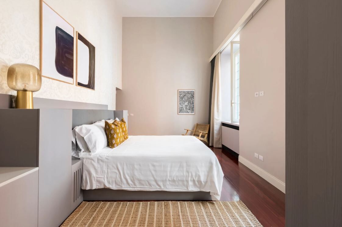A bedroom with a bed, a bedside table, a chair, and artwork on the walls.