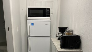 Eine kleine Küche mit einem weißen Kühlschrank, einer Mikrowelle, einem Toaster und einer Kaffeemaschine auf einer Ablagefläche.