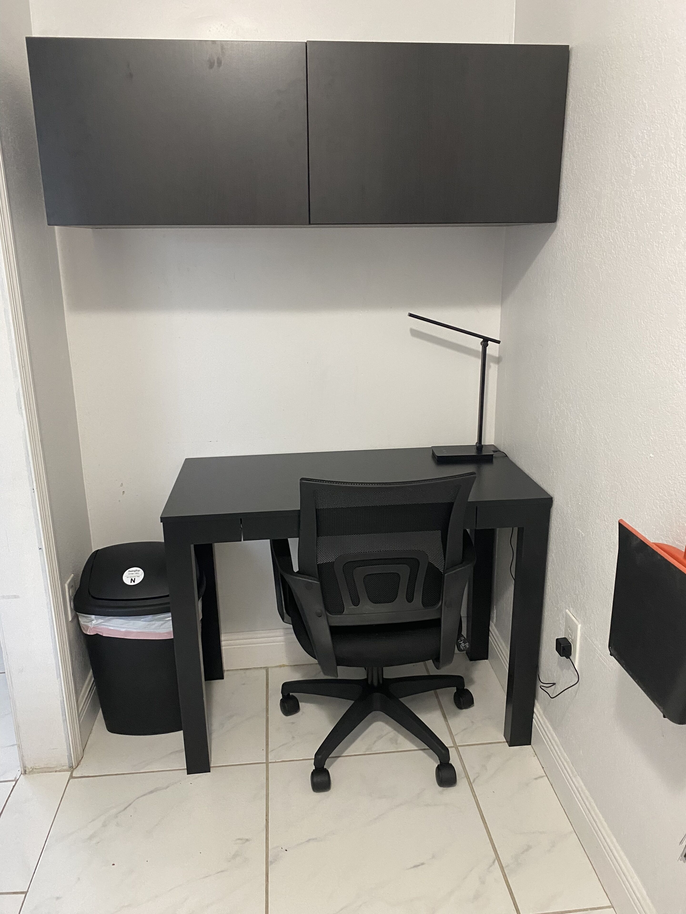 Un piccolo ufficio con scrivania, sedia e cestino.