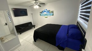 Ein Schlafzimmer mit einem Bett, einer schwarzen Couch, einem Deckenventilator und einem an der Wand befestigten Fernseher.