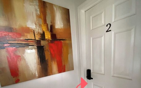 A hallway with a large abstract painting on the wall, a white door with the number 2, and a red arrow pointing towards the door.