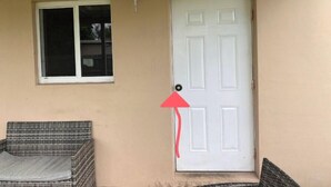 Eine beige Wand mit einer weißen Tür, einem Fenster und einem Korbstuhl.