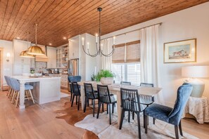 Una cocina moderna con una isla central, comedor con sillas y una lámpara de araña.