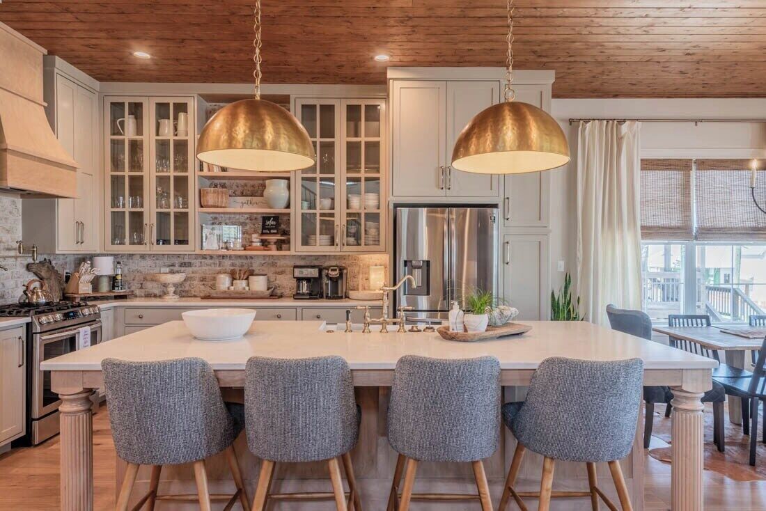 A kitchen with a central island, bar stools, pendant lighting, and a stainless steel refrigerator.