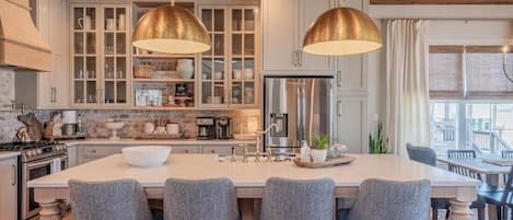 A kitchen with a central island, bar stools, pendant lighting, and a stainless steel refrigerator.