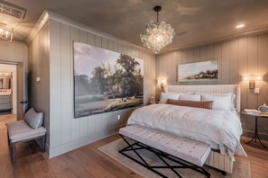 Un dormitorio con una cama grande, un banco, una araña y dos lámparas de pared.
