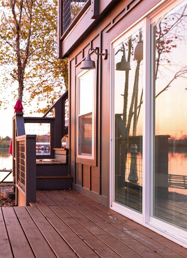 A wooden deck with a railing, a large sliding glass door, and a bell on the wall.