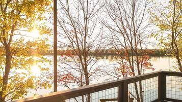 Une vue sur un lac, avec des arbres aux couleurs automnales, une terrasse en bois et une rambarde en métal.