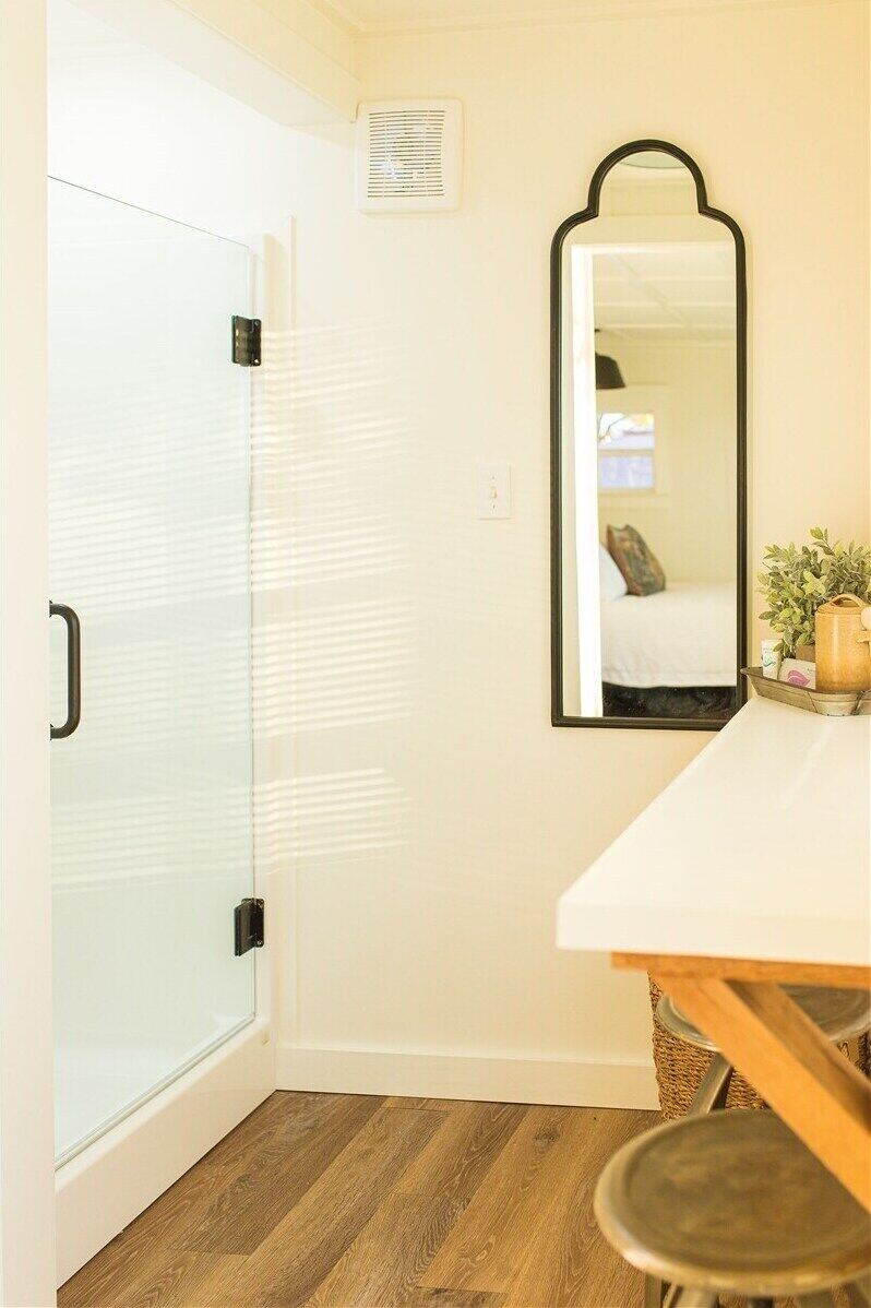 A room with a sliding glass door, a mirror on the wall, a white countertop, and a wooden floor.