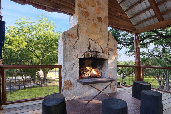 An outdoor stone fireplace with a fire, surrounded by wooden benches and a metal railing.