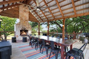 Une terrasse extérieure avec une table et des chaises en bois, une cheminée en pierre et un barbecue.