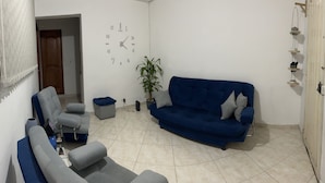 Ein Wohnzimmer mit einem blauen Sofa, grauen Sesseln, einem kleinen Tisch und einer Topfpflanze.
