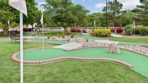 Un campo da minigolf con erba verde, bordi in mattoni rossi e diversi ostacoli.