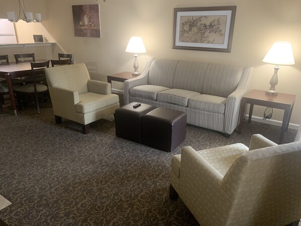 A living room with a sofa, armchairs, a coffee table, and a dining area with chairs and a table. There are two lamps on side tables and a painting on the wall. - Top choice for families. 2BDR/2BA -sleeps 6- at Powhatan Resort. (Williamsburg)