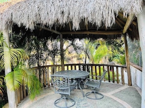 A covered outdoor seating area with a table and chairs, surrounded by a wooden fence and tropical vegetation. - Villa Martha Garza Blanca with Chef & Full Staff (Puerto Vallarta)