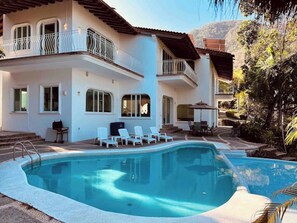 Uma casa de dois andares com piscina, área de estar externa e vista para a paisagem ao redor.