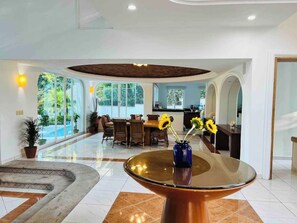 A spacious lobby with a central glass table, seating area, and large windows offering a view of greenery. - Villa Martha Garza Blanca with Chef & Full Staff (Puerto Vallarta)