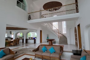 Um interior amplo com escada que leva a um andar superior, área de jantar e sala de estar com sofás.