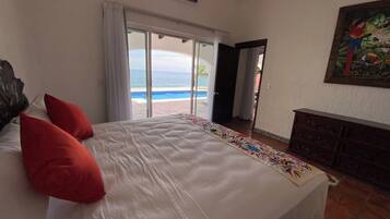A hotel room with a bed, a view of the beach, and a painting on the wall.