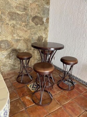 A corner with a stone wall, a tiled floor, and a round table with four stools. - Hacienda + Condo 4: Oceanfront, Sleeps 18 (Aguacate)