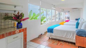 A hotel room with two beds, a tiled floor, a window with a view, a small kitchen area, and a decorative plant.