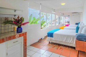 A hotel room with two beds, a tiled floor, a window with a view, a small kitchen area, and a decorative plant.