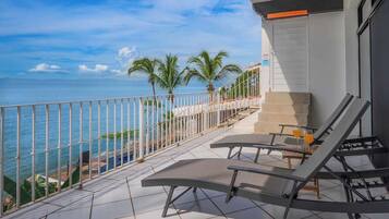 A balcony with a view of the sea, two lounge chairs, and a small table with drinks.