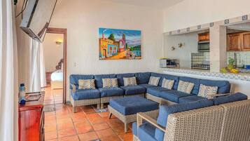 A living room with a large sectional sofa, a kitchen area with a tiled backsplash, and a painting on the wall.